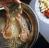 Adding sage leaves to a pan of fried lamb cutlets