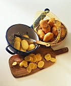 Potatoes in net and strainer and slices on chopping board