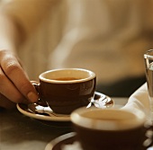 Hand holding an espresso cup on table