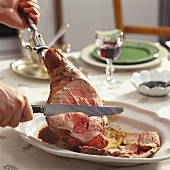 Carving leg of lamb on laid table