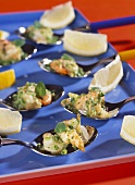 Shrimps with oregano on spoons; lemon wedges