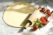 Rolled-out pizza dough, tomato sauce and fresh tomatoes
