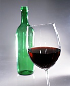 Red wine in glass in front of green bottle