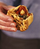 Hand holding vegetable pie with a bite taken