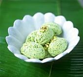 Pistachio ice cream in white bowl on banana leaf