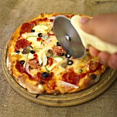 Vegetable pizza with ham; hand with pizza cutter