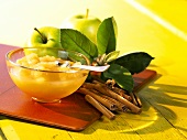 Apple compote in bowl; cinnamon sticks; fresh apples