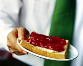 Hand holding plate of jam with bread