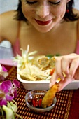 Woman dipping spring roll in soy sauce
