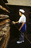 Female baker taking bread out of the oven in the bakery