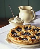 A blueberry tart with a bowl of whipped cream beside it