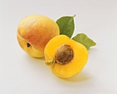 A half and a whole apricot with leaves