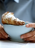 Hands holding bowl with croissant