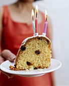 Frau serviert Stück Geburtstagsgugelhupf mit drei Kerzen