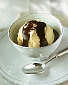 Vanilla ice cream with chocolate sauce in small white bowl