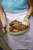 Woman holding bowl of barbecued sausages