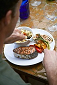 Man eating barbecued salmon cutlet with vegetables