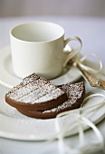 Pieces of chocolate cake with icing sugar beside coffee cup