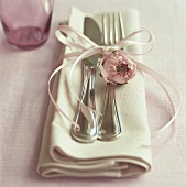 Silver cutlery with bow and pink flower on fabric napkin