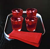 Water and ice cubes in red glasses on tray