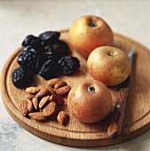 Apples, prunes and almonds on wooden board
