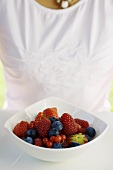 Assorted berries in white bowl, woman in background