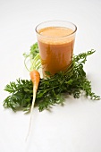 Glass of carrot juice and fresh carrot with leaves