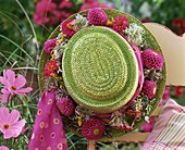 Green straw hat with wreath of dahlias on garden chair