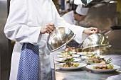 Female chef covering main courses with domed covers