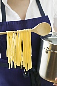 Woman holding pan and home-made pasta on wooden spoon
