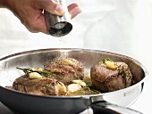 Seasoning fillet steaks in frying pan