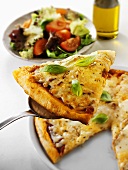 Stück Pizza mit Käse auf Heber, Salatteller im Hintergrund