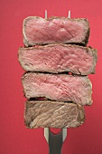 Slices of beef steak on carving fork (different degrees of cooking)