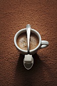 Cup of espresso and spoon with sugar cube on coffee powder