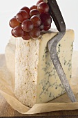 Piece of Stilton with red grapes and cheese knife on paper