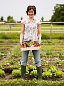 Woman holding crate of freshly picked vegetables in garden