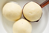 Three potato dumplings in water with ladle (overhead view)