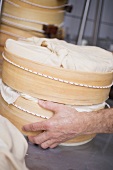 Hand holding wrapped cheeses in round wooden moulds