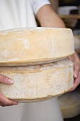 Person holding two large cheeses (Almkäse, Alpine cheese)