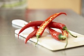 Red chillies, whole and halved, on chopping board