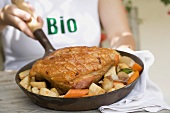 Woman holding pan of organic roast pork & root vegetables