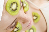 Young woman with slices of kiwi fruit on her face and neck