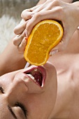 Junge Frau presst Saft aus eine Orange in ihren Mund