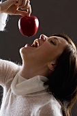 Young woman holding an apple above her mouth