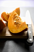 Pumpkin wedges with knife on wooden board