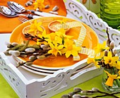 Oranger Teller mit Narzissen, Palmkätzchen und Haselzweig