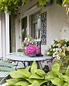 Blumenschmuck auf verwittertem Gartentisch vor einem Landhaus