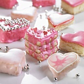 Several heart-shaped petit fours with pink icing and silver dragees