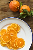 Teller mit Orangenscheiben und Orangen mit Blättern