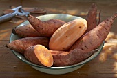 Sweet potatoes in a bowl, whole, halved and peeled
